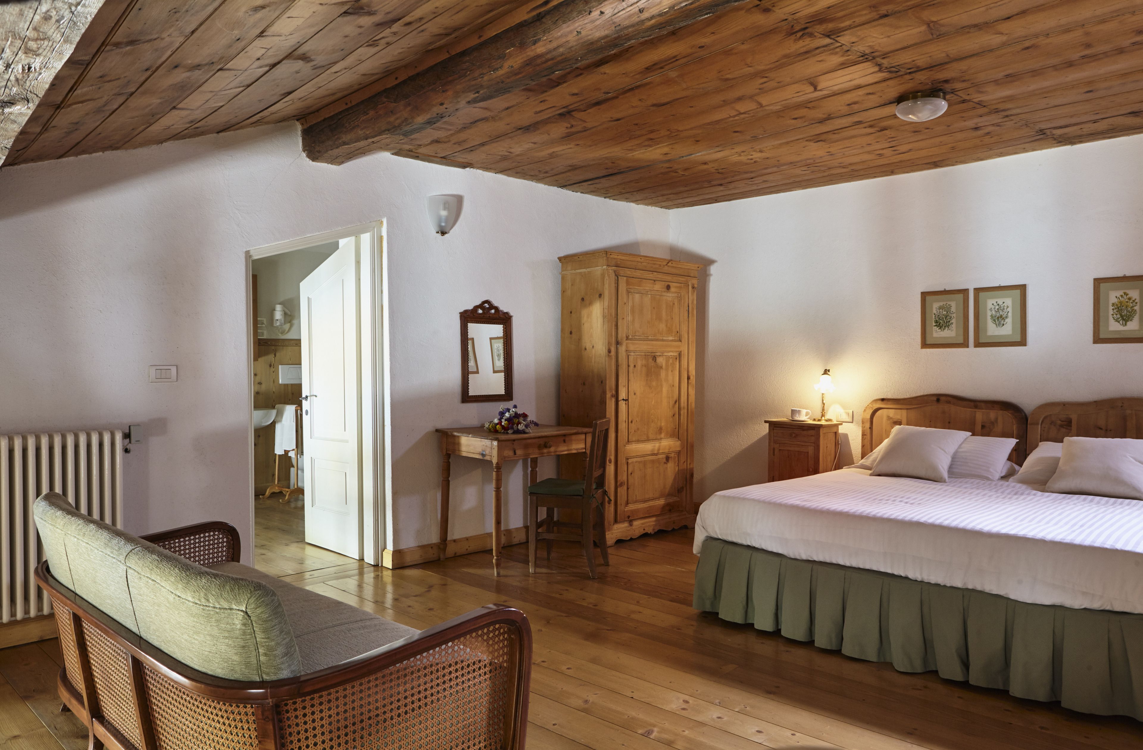 Een slaapkamer met een houten plafond, een bed met wit beddengoed, een houten garderobe, een houten tafel met een stoel, en een radiator.