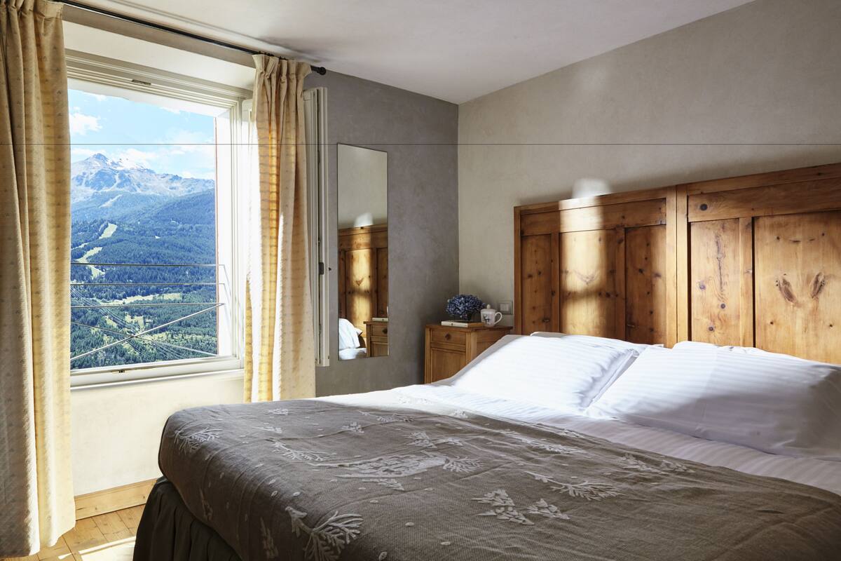 Ein Schlafzimmer mit einem großen Bett, einem Holz-Kopfteil, einem Nachttisch, einem Spiegel und einem Fenster mit Blick auf Berge.