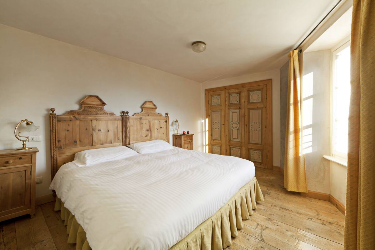 Ein Schlafzimmer mit einem hölzernen Bett, einem Nachttisch, einer Kommode und einem Fenster mit Vorhängen.