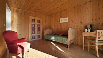 Une pièce de cabane en bois comprenant un lit, une chaise rouge, une table et une porte en bois ornée de panneaux décoratifs.