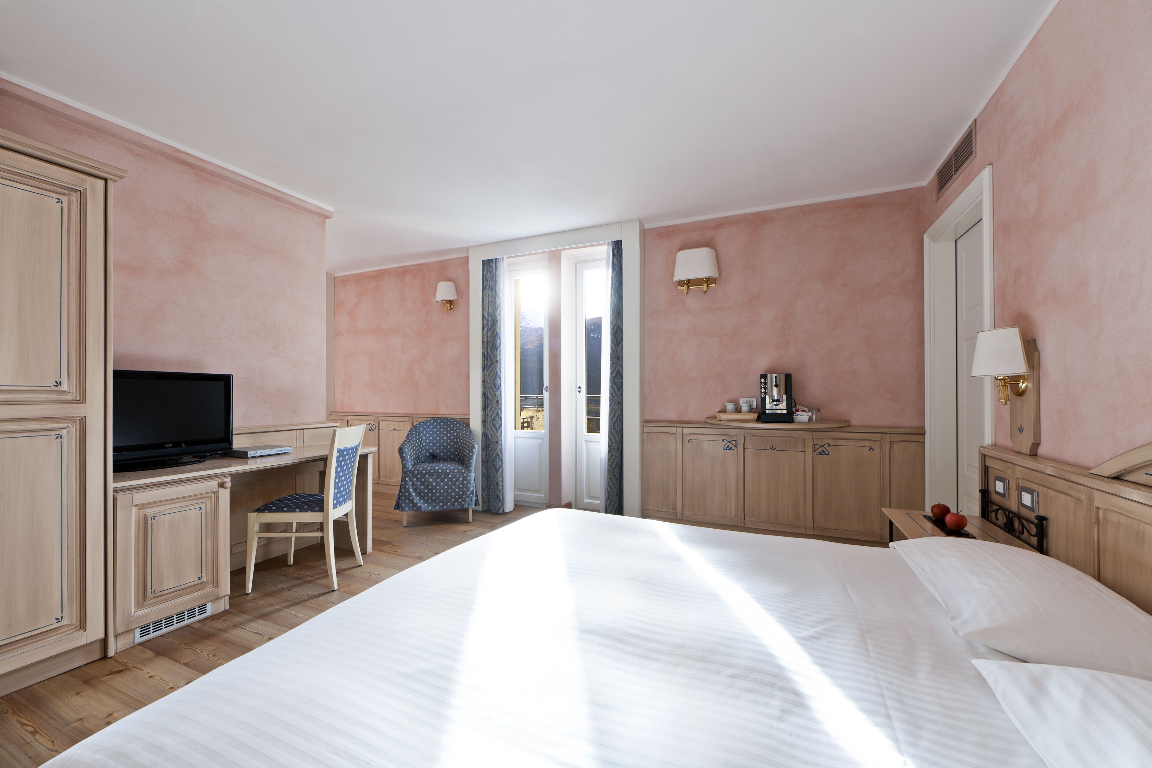 Une chambre d’hôtel comprenant un lit, un bureau avec une télévision, une chaise, une lampe de bureau et une fenêtre avec des rideaux.