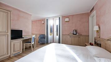 Une chambre d’hôtel comprenant un lit, un bureau avec une télévision, une chaise, une lampe de bureau et une fenêtre avec des rideaux.