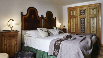 Una cama bien hecha con cabecera de madera, una mesita de noche con una lámpara y una cortina verde.