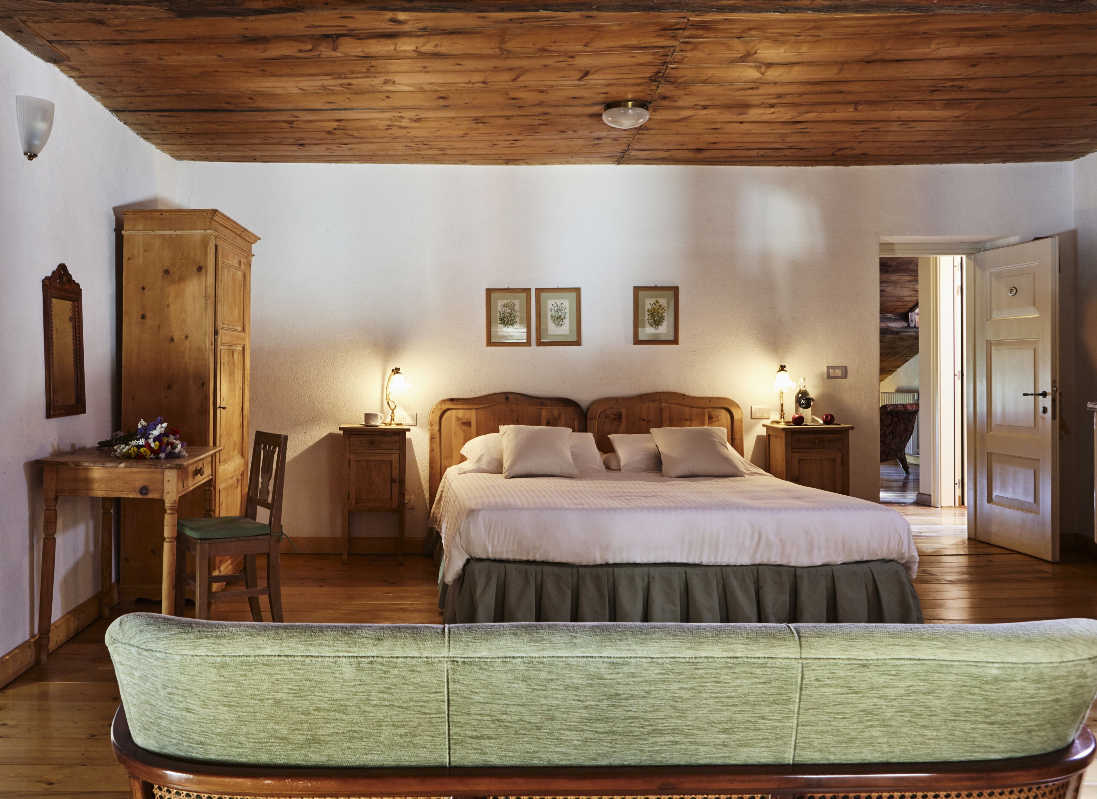 Una camera da letto con soffitto in legno, un letto con lenzuola bianche, un comodino in legno, una poltrona imbottita verde e un armadio in legno.