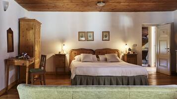 Quarto com teto de madeira, cama com roupa de cama branca, mesa de cabeceira de madeira, cadeira estofada verde e guarda-roupa de madeira.
