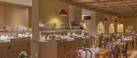 A restaurant with wooden interiors, a central island with dishes, and red pendant lighting.