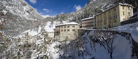 A snow-covered mountain landscape with a building featuring multiple windows and balconies, surrounded by trees and snow.