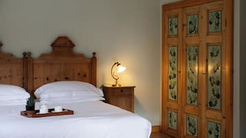 A bedroom with a wooden headboard, a bedside table with a lamp, a tray with a plant and two cups, and a large wooden door with glass panels.