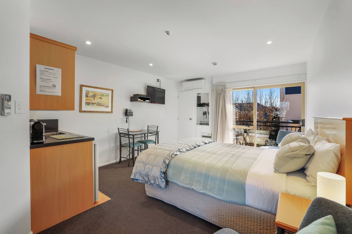 A hotel room with a bed, a desk, a chair, a television, and a window with a view of trees.