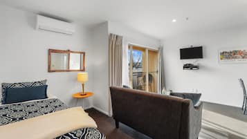 Une chambre d’hôtel avec un lit, un canapé, une télévision et un balcon avec des rideaux.