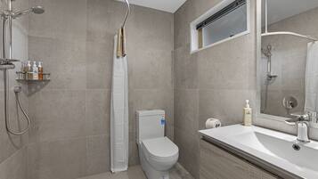 Een moderne badkamer met toilet, douche en wastafel.