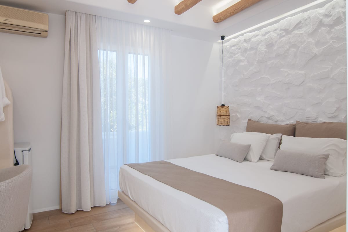 A bedroom with a large bed, a hanging light fixture, and a white textured wall.