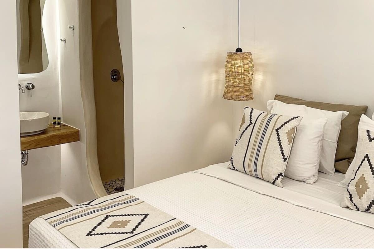 A bedroom with a bed, a hanging light fixture, a mirror, and a wooden shelf.