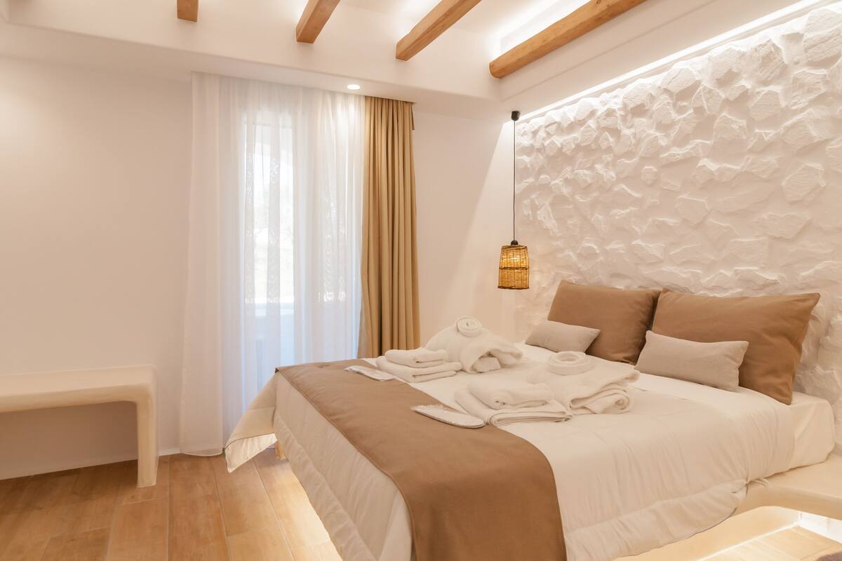 A modern bedroom with a large bed, a bench, and a textured wall.