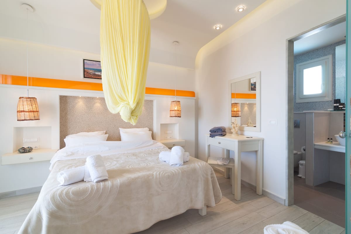 A modern hotel room with a large bed, bedside tables, a desk, and a bathroom visible through an open door.