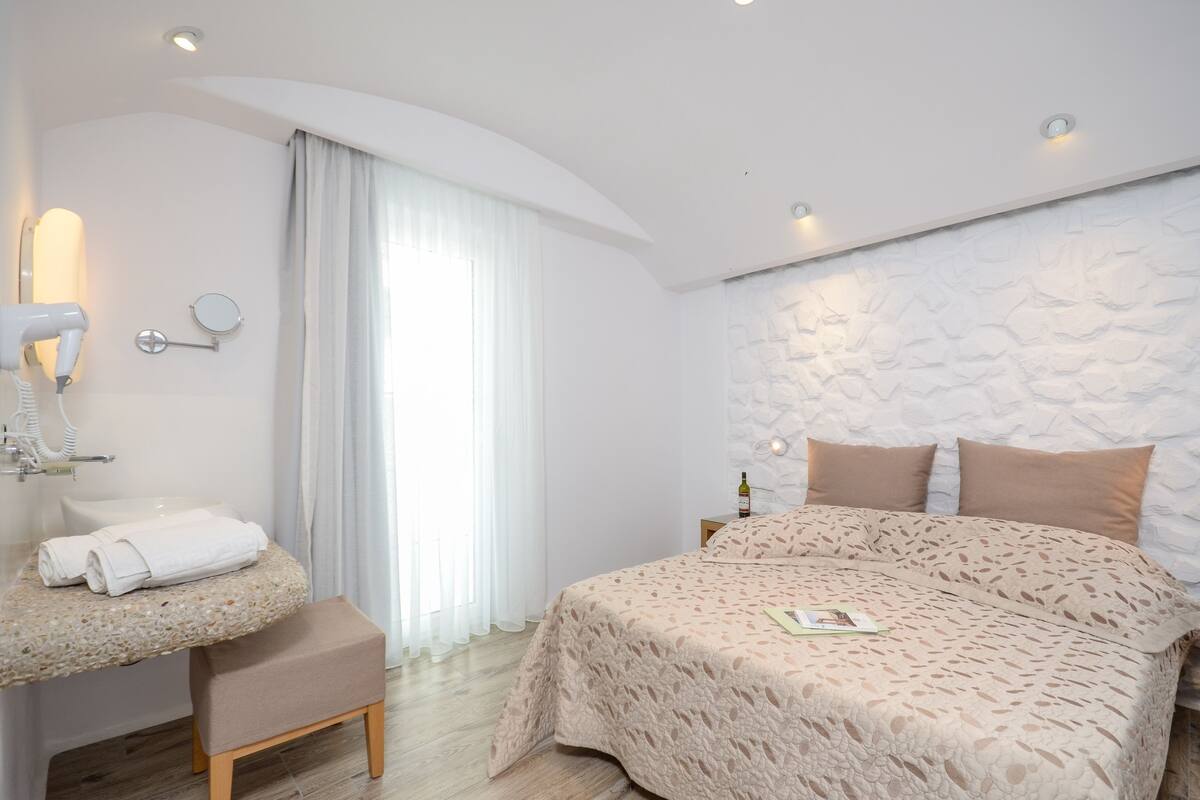A bedroom with a bed, a vanity with a mirror, a hairdryer, and a bottle of wine on the nightstand.
