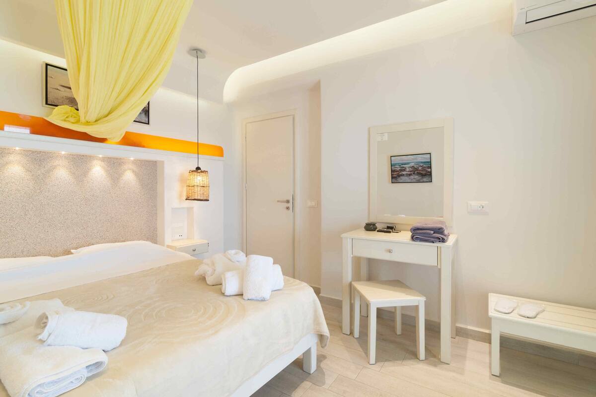 A hotel room with a bed, a desk, a bench, and a hanging yellow curtain.