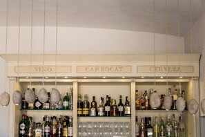 A bar area with shelves labeled VINO, CAP ROCAT, and CERVEZA, displaying various bottles and glasses.