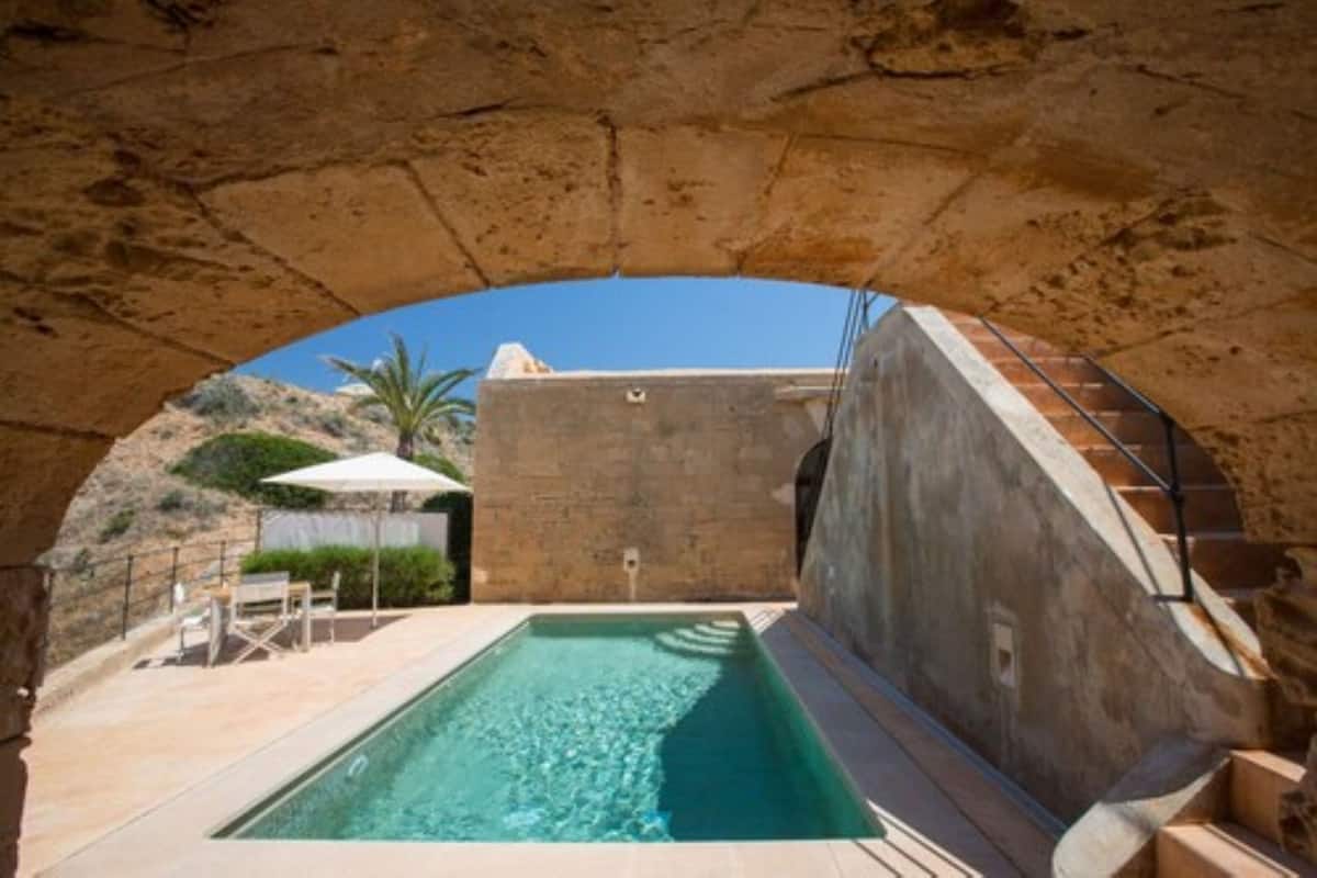 A swimming pool with a stone archway, a staircase, and outdoor seating.