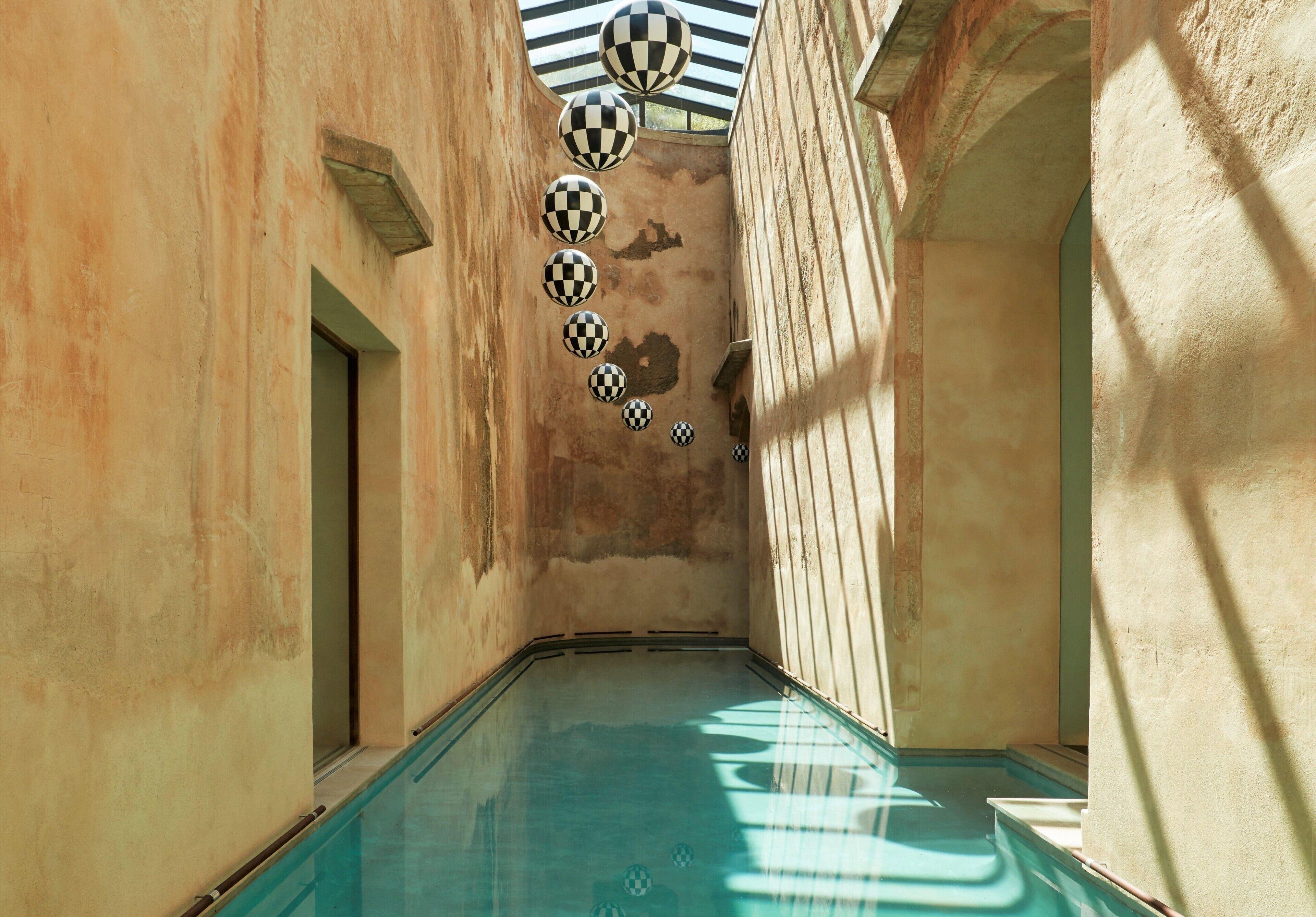 Una piscina interior estrecha con bolas a cuadros colgando del techo, rodeada de paredes con textura.