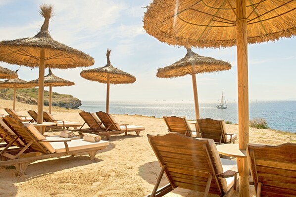 A beachside lounge area with wooden lounge chairs and thatched umbrellas, overlooking the sea. - Cap Rocat (Llucmajor)