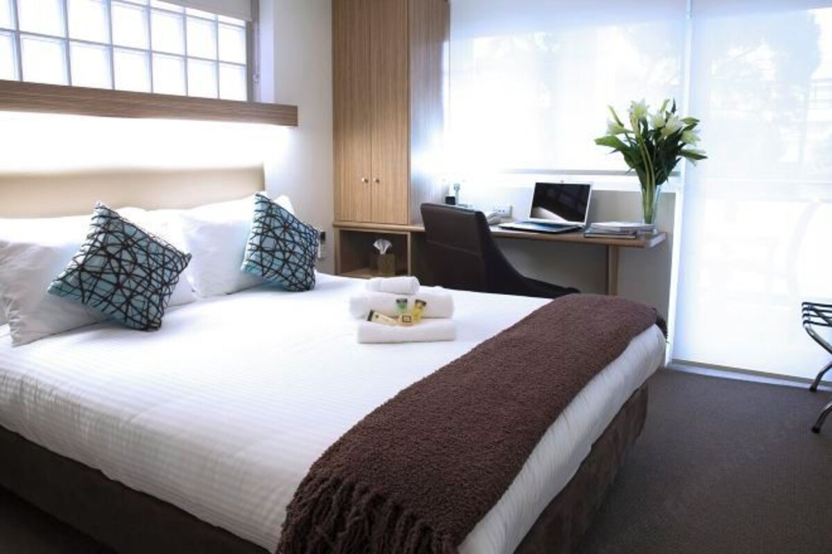 A hotel room with a bed, a desk with a laptop, a chair, and a window with a view.