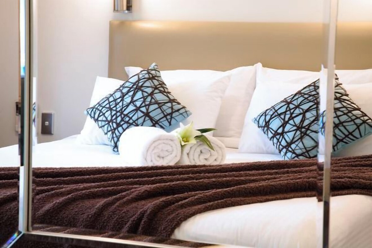 A neatly made bed with white linens, two patterned pillows, and a brown throw blanket.