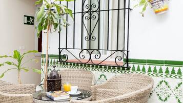 Un rincón de descanso de mimbre con una mesa, sillas, un libro, un vaso de jugo de naranja y un farol decorativo.