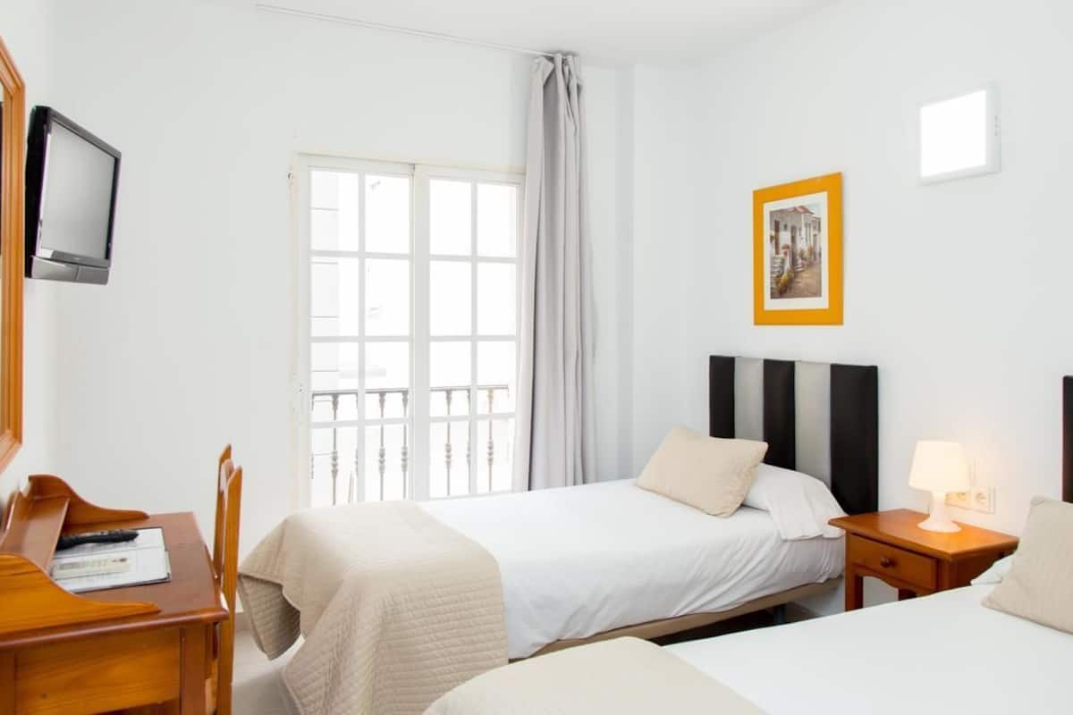 A hotel room with two beds, a desk, a chair, a TV, and a window with curtains.