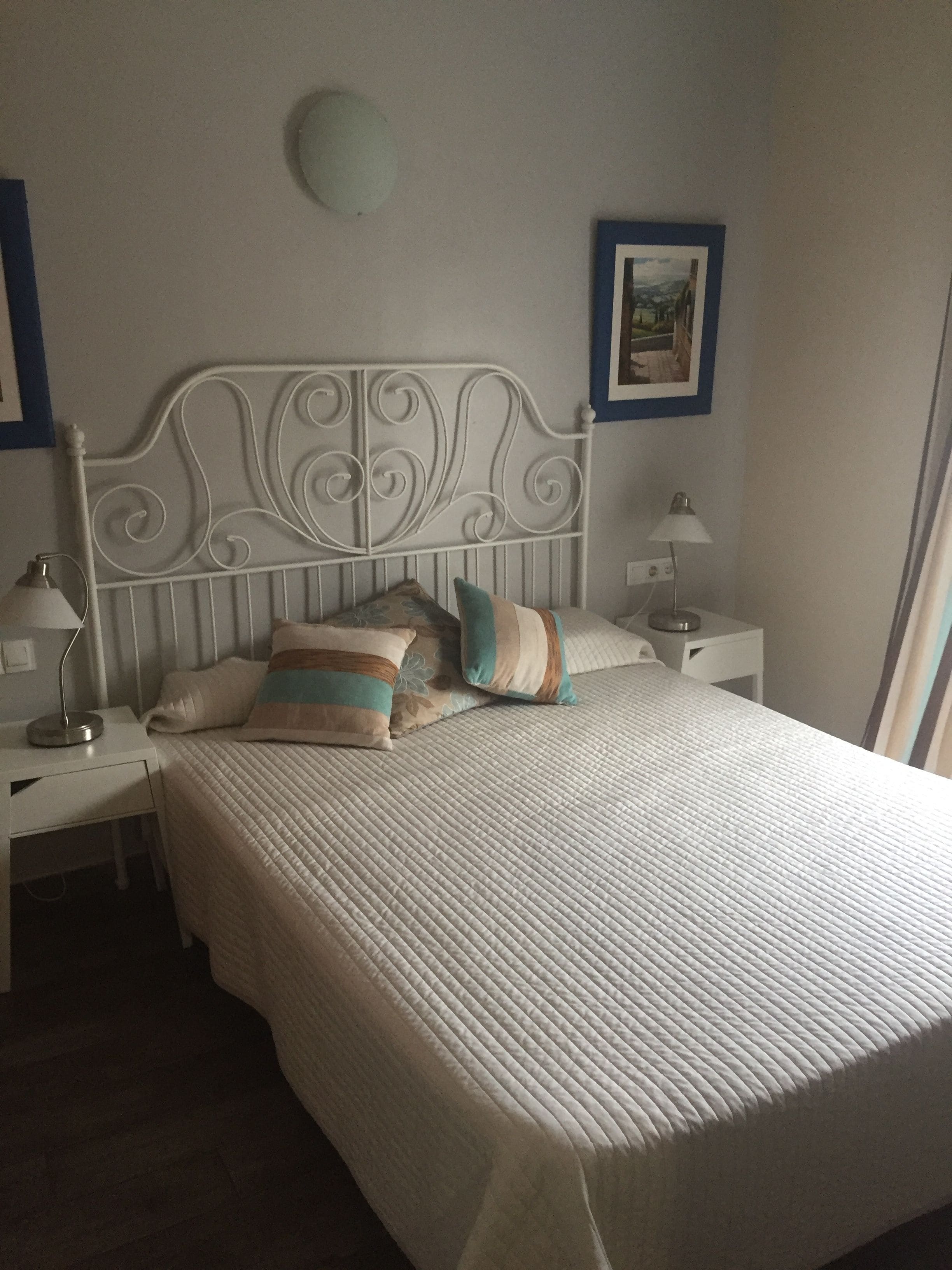 Ein ordentlich bezogenes Bett mit einem weißen Kopfteil, zwei Nachttischen mit Lampen und einem gerahmten Bild an der Wand.