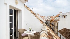 Un balcón con mobiliario de mimbre, una pequeña mesa con una flor y vistas a una hilera de edificios.