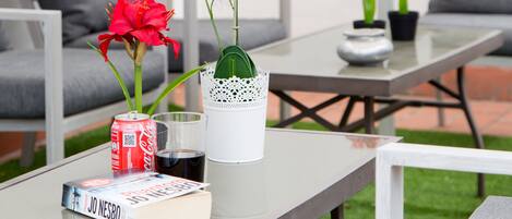 A patio area with outdoor furniture, a table with books and a soda can, and potted plants.