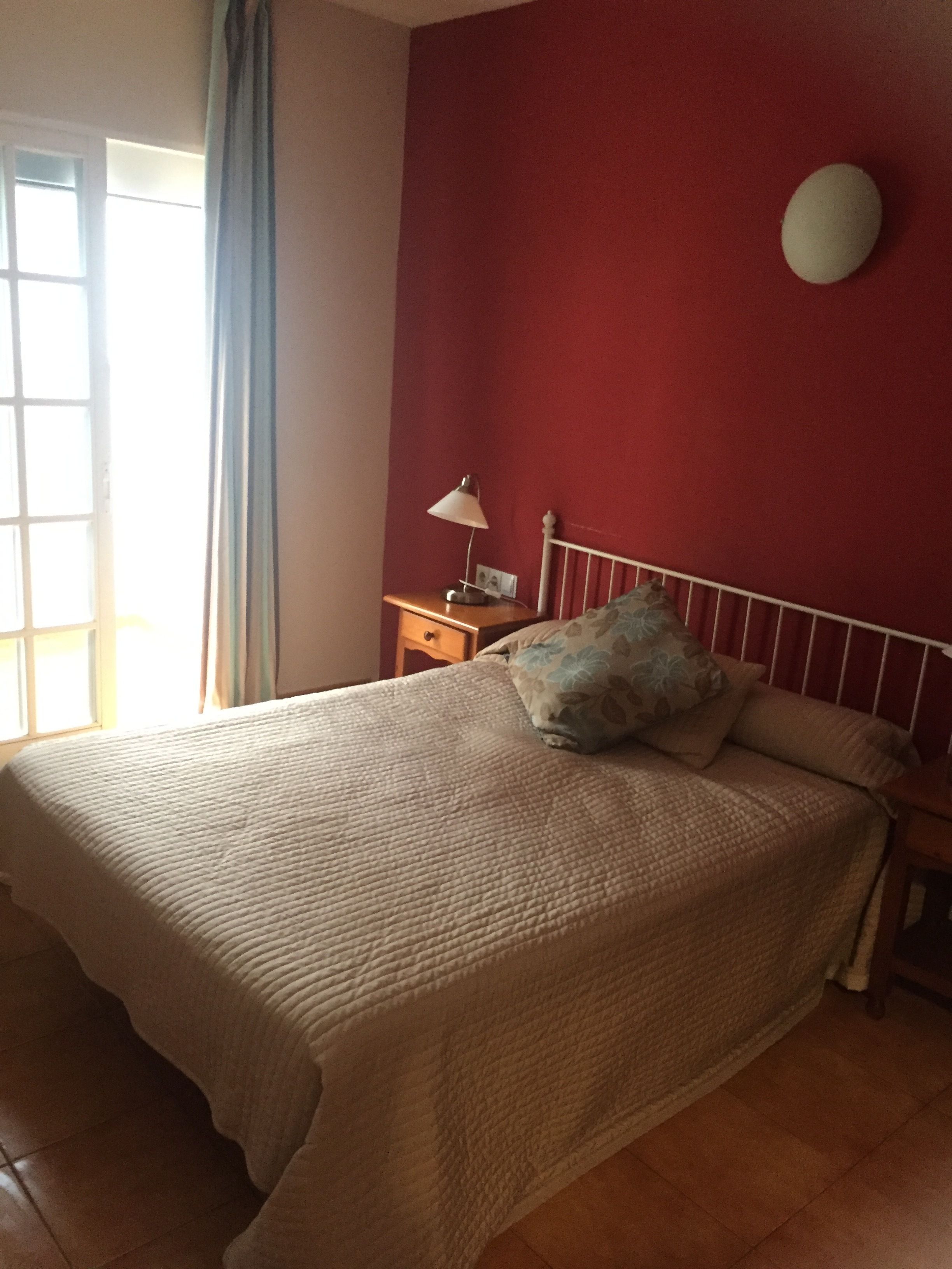 Une chambre à coucher avec un lit, une table de chevet, une lampe et une fenêtre avec des rideaux.