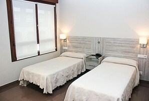 A hotel room with two single beds, a small table, two wall-mounted lamps, and a window with blinds. - Hotel Playa Poniente (Gijon)