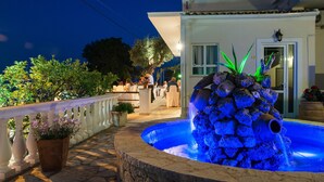 Un espace extérieur aménagé pour la nuit, comprenant un élément aquatique, des sièges et l’entrée d’un bâtiment.