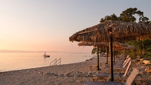 Une plage avec des parasols en chaume, des chaises longues et un bateau sur l’eau.