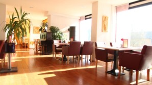 Un comedor amplio con una mesa larga y varias sillas, rodeado de plantas en macetas y una chimenea.