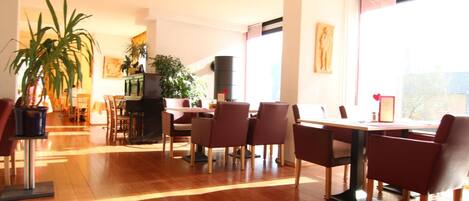 A spacious dining area with a long table and multiple chairs, surrounded by potted plants and a fireplace.