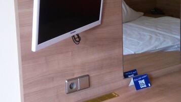 Ein Hotelzimmer mit einem an der Wand befestigten Flachbildfernseher, einem Nachttisch mit einem Buch und einem Bett mit weißer Bettdecke.