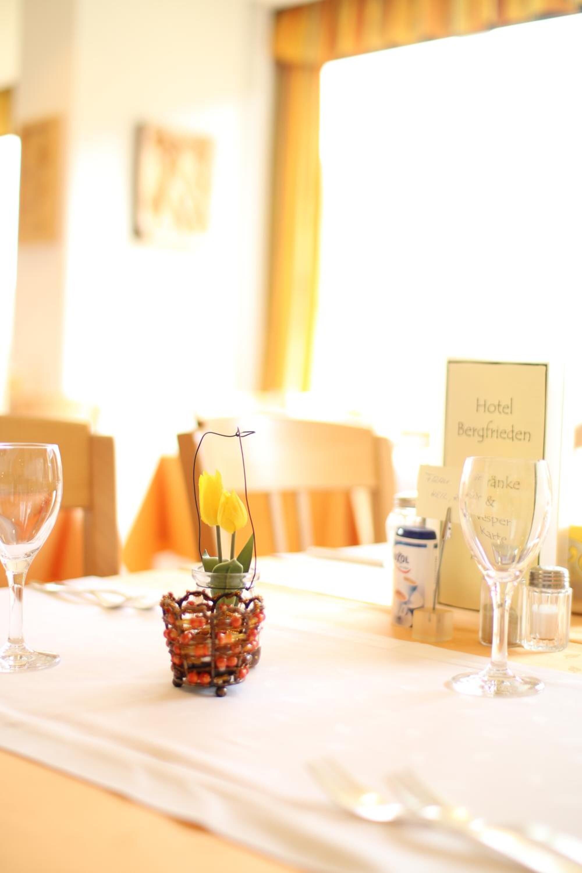 A hotel room with a neatly arranged table featuring a glass vase with yellow flowers, a menu sign, and a bottle of water.