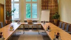 Un salón de conferencias con una larga mesa, sillas, una pizarra y plantas en macetas.