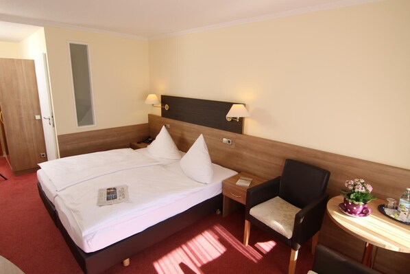 A hotel room with a bed, bedside table, chair, and a small table with a plant.