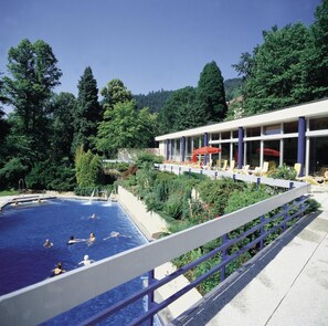 Una piscina con gente, rodeada de vegetación exuberante y un edificio con terraza.