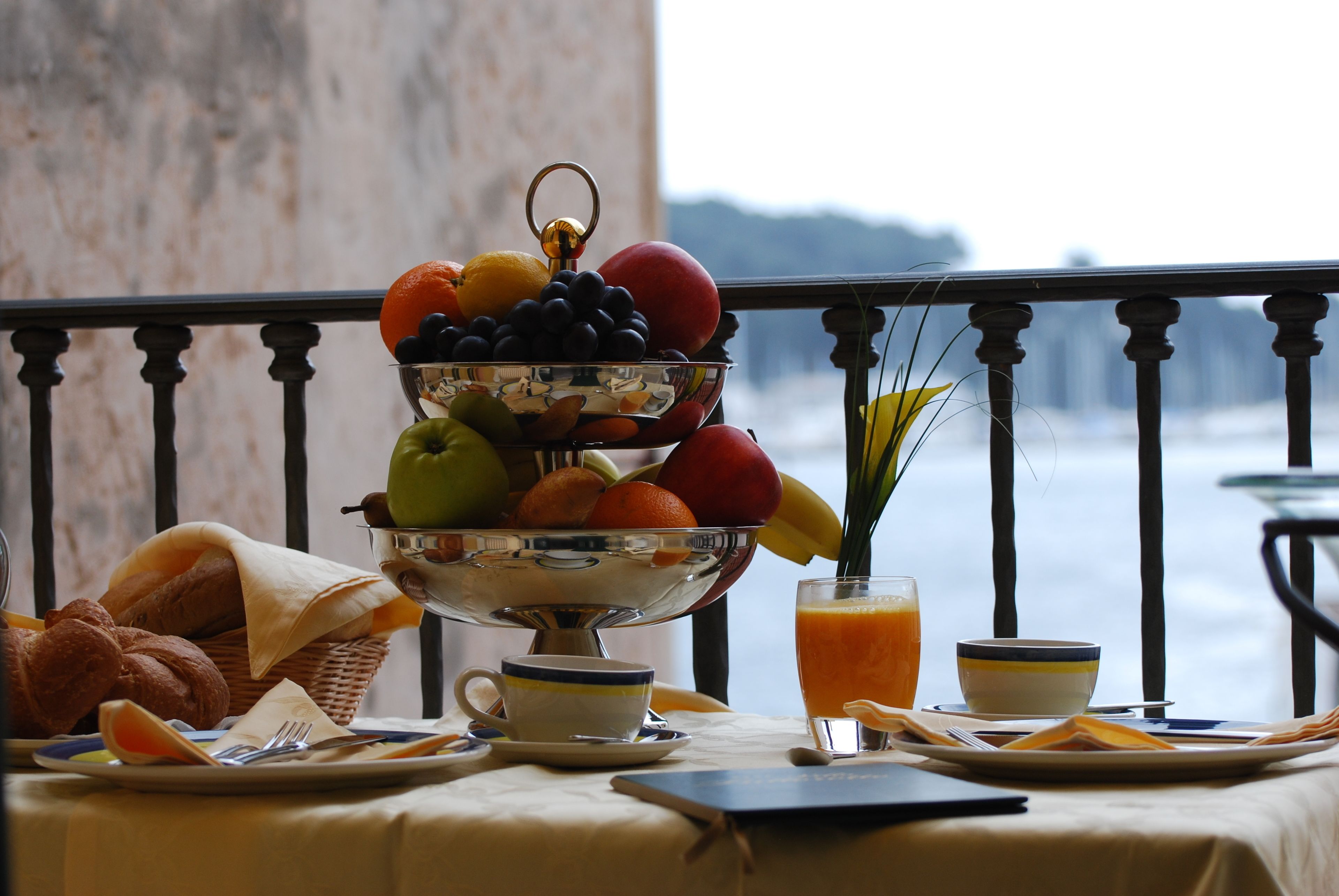 A breakfast table with a fruit bowl, croissants, and a glass of orange juice.