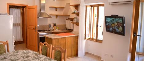 Une cuisine compacte avec des étagères en bois, un coin repas avec une table et des chaises, et un téléviseur fixé au mur.