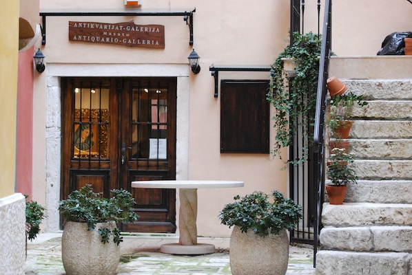 A courtyard with a stone table and planters, a wooden door, and a sign above the door.
