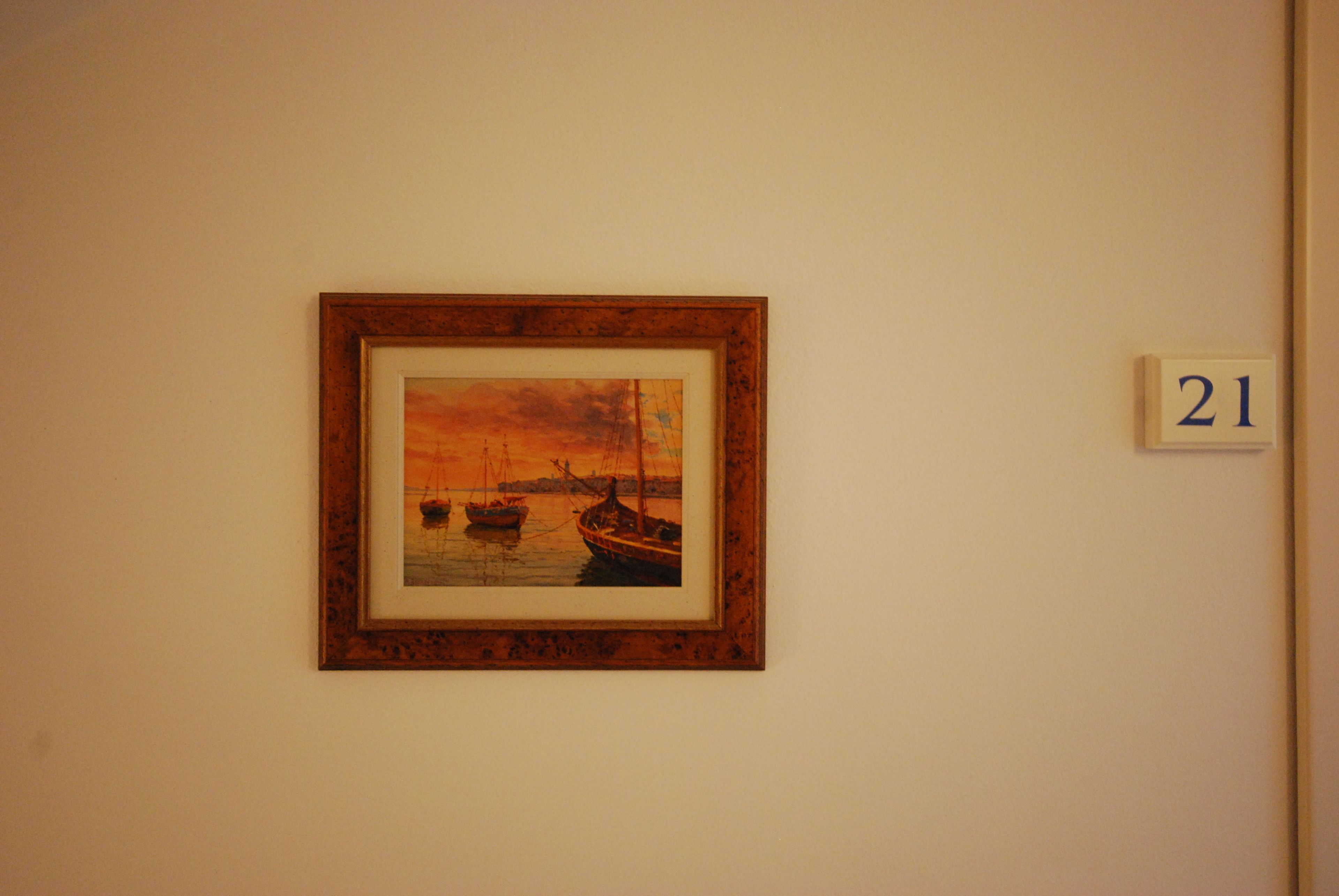 A framed painting of boats on water, a number plaque, and a plain wall.