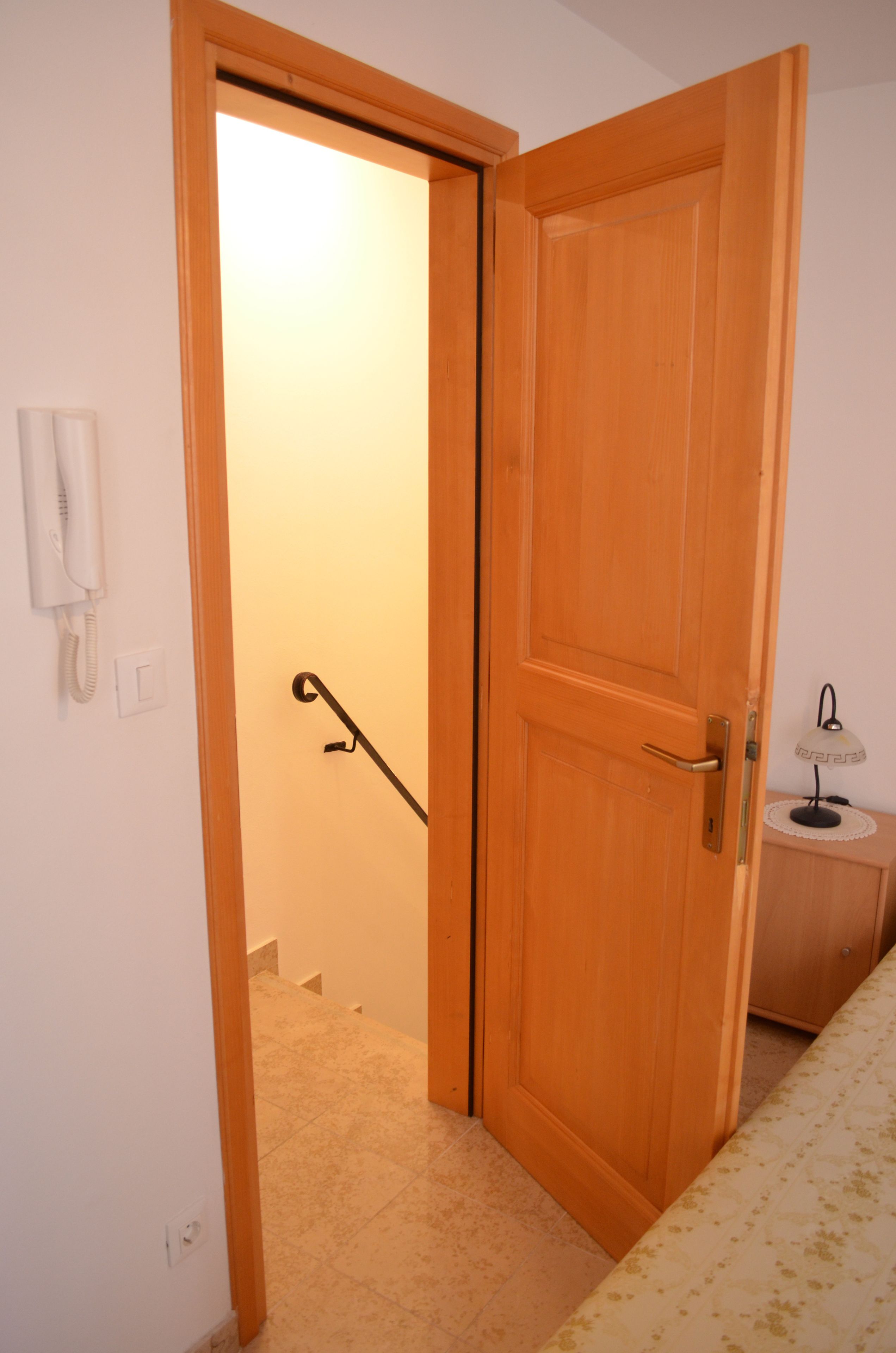 Eine Holztür, die in einen Raum führt, der einen Telefon, eine Lampe und einen gemusterten Teppich enthält.