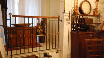 Ein Zimmer mit einem Holzstuhl, einem Metallgeländer, einer Uhr und verschiedenen antiken Gegenständen auf Regalen.