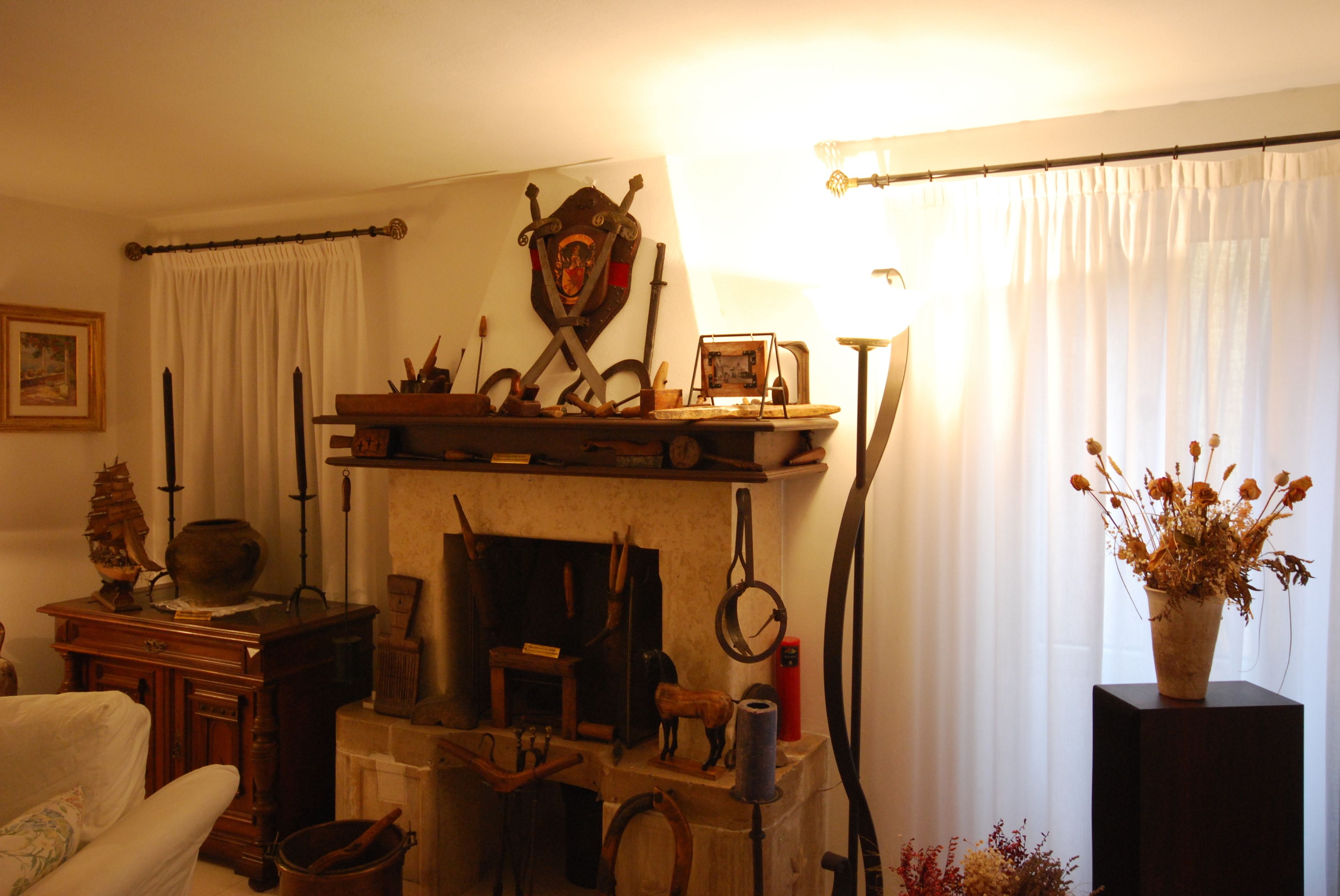 Une pièce avec une cheminée, une étagère en bois sur laquelle sont disposés divers objets, un tableau encadré et un vase contenant des fleurs séchées.